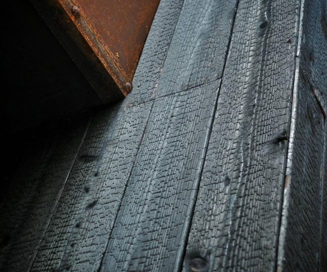 Close up of Yakisugi a.k.a Shousugiban charred cedar cladding next to weathered steel architectural detail.
