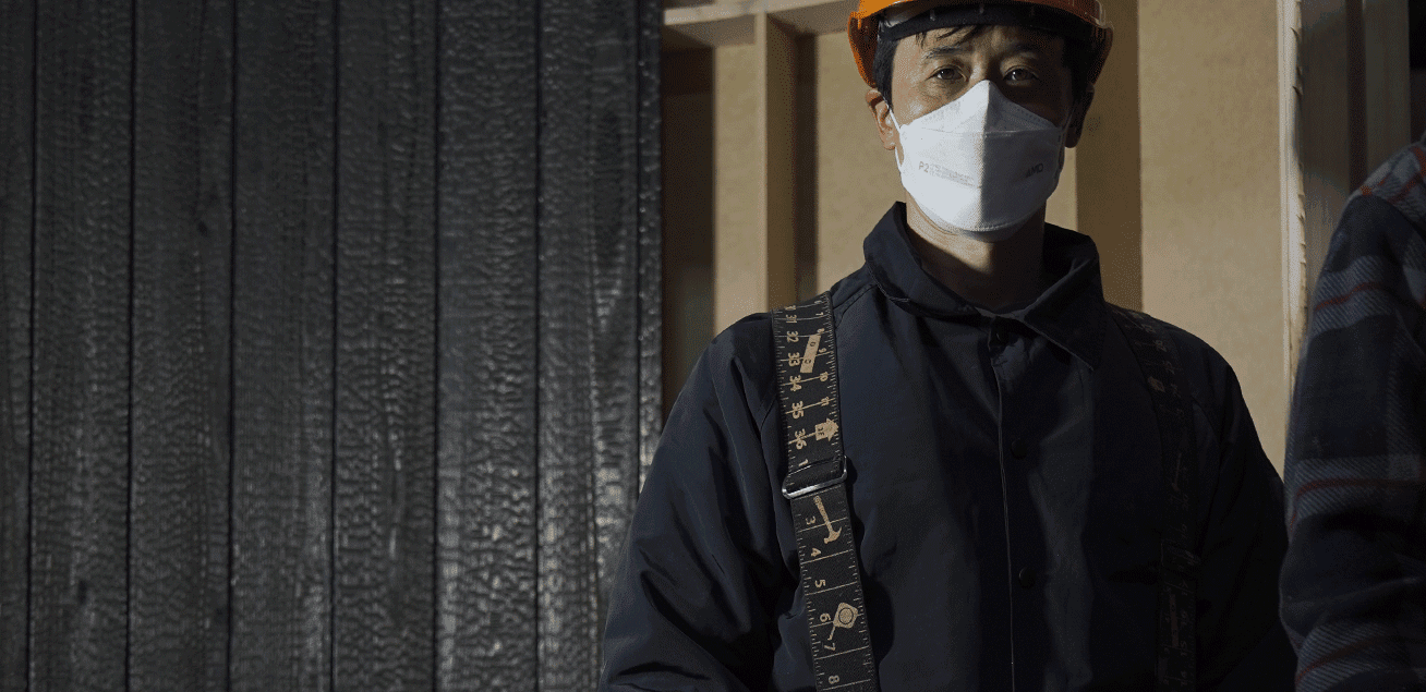 Professional installer standing beside Yakisugi a.k.a Shousugiban charred cedar cladding during construction.